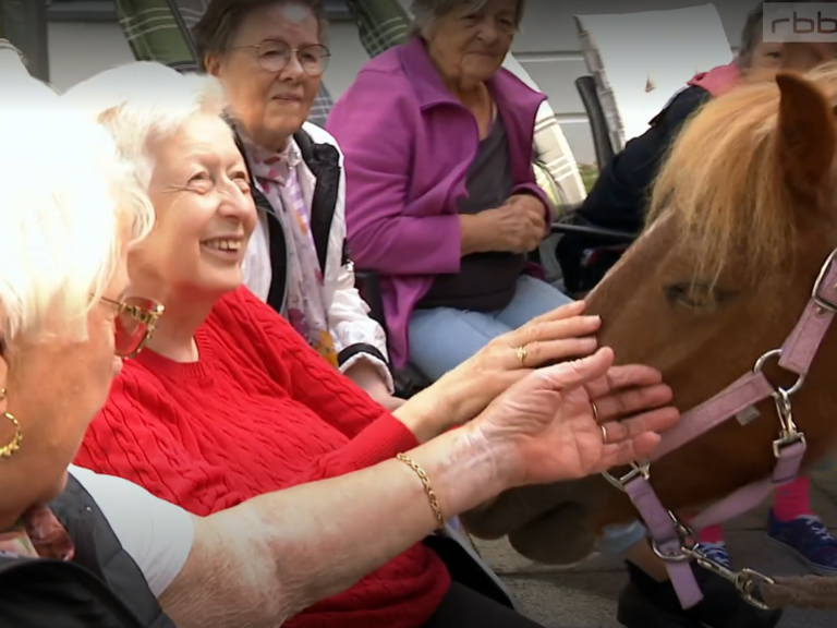 Screenshot aus der Sendung des rbb mit zwei Bewohnerinnen, die das Pony am Kopf streicheln