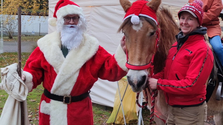 Der Weihnachtsmann bringt festliche Freude während ein geschmücktes Pferd über den Weihnachtsmarkt geführt wird - Immanuel Haus Ecktannen