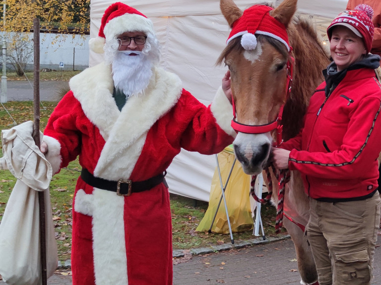 Der Weihnachtsmann bringt festliche Freude während ein geschmücktes Pferd über den Weihnachtsmarkt geführt wird - Immanuel Haus Ecktannen