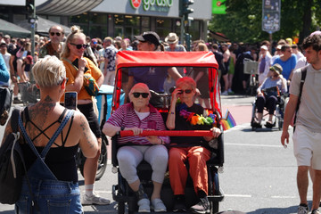 Eine rote Rikscha mit zwei Fahrgästen inmitten einer Menschenmenge beim Besuch des Christopher Street Days in Berlin 2026 vom Immanuel Seniorenzentrum Schöneberg. Eine rote Rikscha mit zwei Fahrgästen inmitten einer Menschenmenge beim Besuch des Christopher Street Days in Berlin 2026 vom Immanuel Seniorenzentrum Schöneberg.
