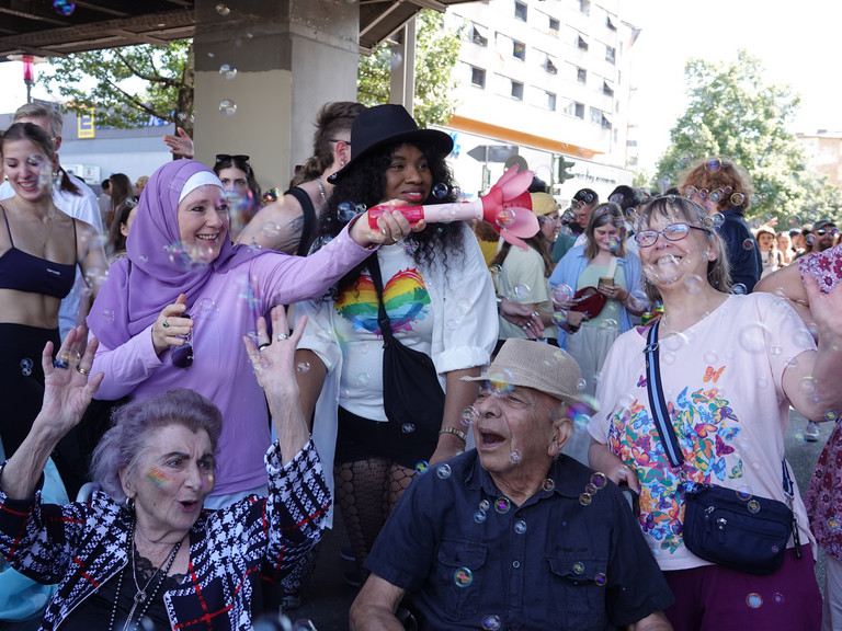 Eine Gruppe fröhlicher Menschen unterschiedlichen Alters mit einer Seifenblasenmaschine beim Besuch des Christopher Street Days in Berlin 2026 vom Immanuel Seniorenzentrum Schöneberg.