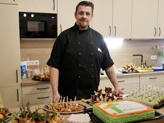 Ein Koch in schwarzer Arbeitskleidung steht hinter dem Kuchen- und Fingerfoodbüffet und blickt in die Kamera bei der Wiedereröffnung der Tagespflegestätte für ältere Menschen im Immanuel Seniorenzentrum Kläre Weist in Petershagen