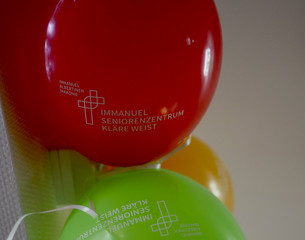 Luftballons in rot, grün und organge mit dem Kreuzbandlogo und dem Namen der Einrichtung bei der Wiedereröffnung der Tagespflegestätte für ältere Menschen im Immanuel Seniorenzentrum Kläre Weist in Petershagen