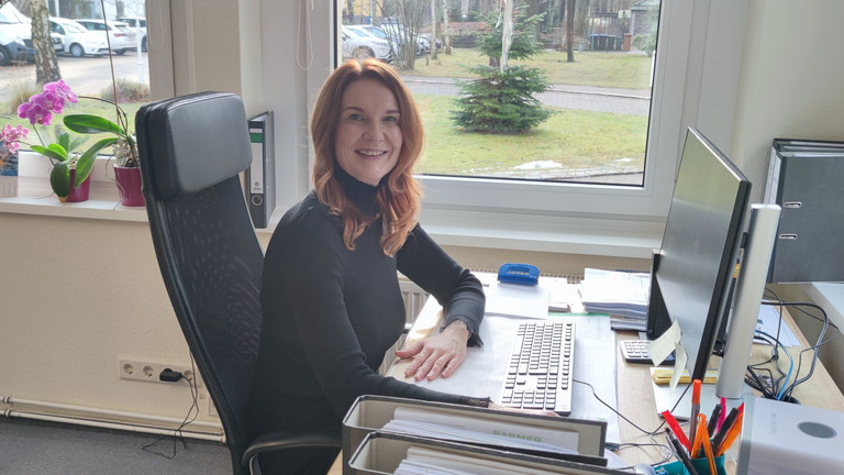 Umschülerin Christina blickt während ihres Praktikums im Immanuel Haus Ecktannen am Schreibtisch mit Monitor sitzend lächelnd in die Kamera