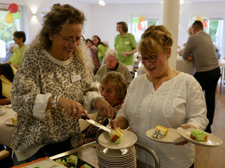 Eine Mitarbeiterin reicht einer Frau Kuchen auf mehrere Teller bei der Wiedereröffnung der Tagespflegestätte für ältere Menschen im Immanuel Seniorenzentrum Kläre Weist in Petershagen