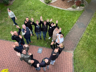 Ein Team von Mitarbeitenden steht im Kreis und blickt nach oben die Kamera zum 25-jährigen Jubiläum des Immanuel Suchthilfeverbunds Guben mit besonderen Wohnformen für abhängigkeitskranke Menschen in Thüringen Ein Team von Mitarbeitenden steht im Kreis und blickt nach oben die Kamera zum 25-jährigen Jubiläum des Immanuel Suchthilfeverbunds Guben mit besonderen Wohnformen für abhängigkeitskranke Menschen in Thüringen