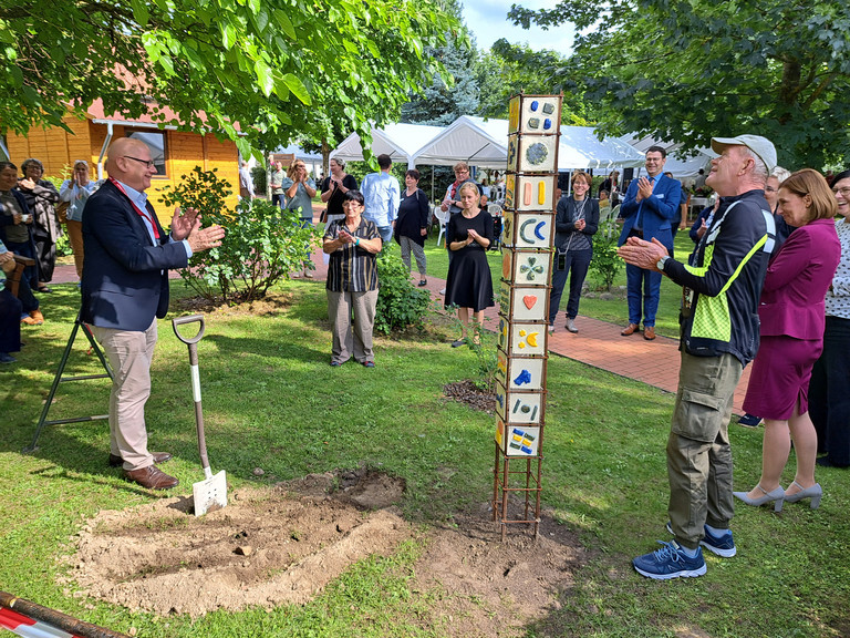 Geschäftsführer Herbert Blum (links) hat für die Nachwelt eine Zeitkapsel bei der von Bewohnenden gestalteten Stele vergraben.