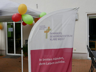 Bunte Luftballons und ein Banner mit dem Kreuzbandlogo der Einchrichtung und dem Text "In besten Händen, dem Leben zuliebe" am Eingang bei der Wiedereröffnung der Tagespflegestätte für ältere Menschen im Immanuel Seniorenzentrum Kläre Weist in Petershagen