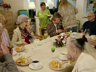 Mehrere Seniorinnen und Senioren sitzen mit Kaffee und Kuchen an einem gedeckten Tisch bei der Wiedereröffnung der Tagespflegestätte für ältere Menschen im Immanuel Seniorenzentrum Kläre Weist in Petershagen